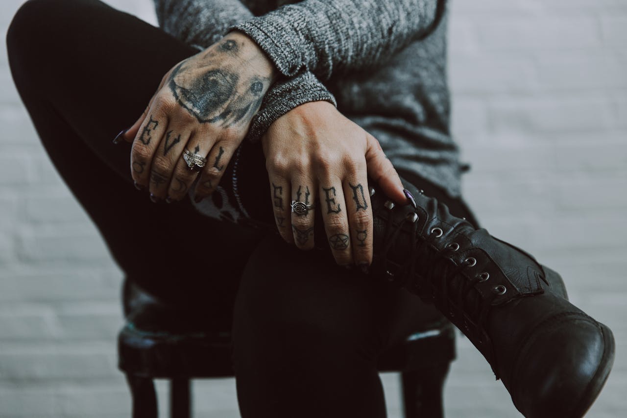 menu-01 Close-up of tattooed hands and rings resting on black boots, creating a moody and artistic vibe.