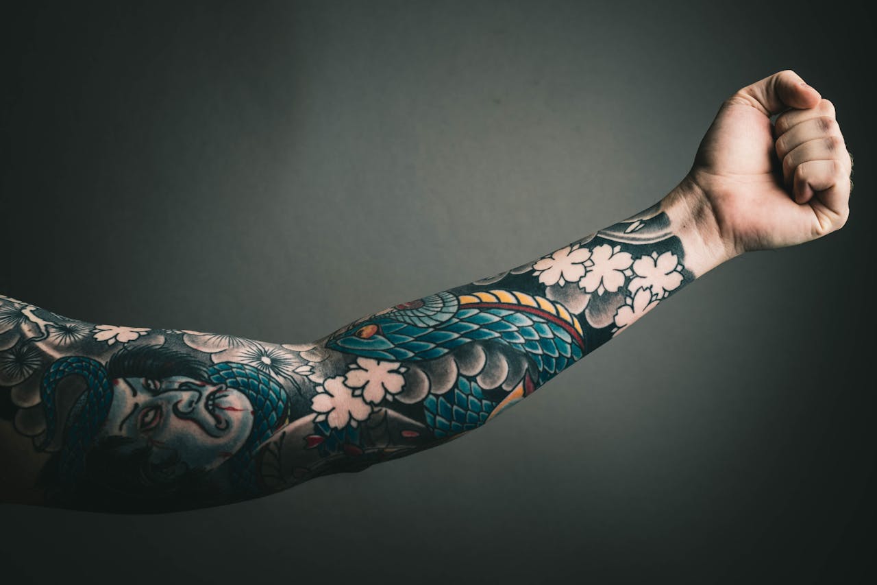 about-03 A close-up of a tattooed arm with a colorful sleeve design, featuring floral and artistic elements.