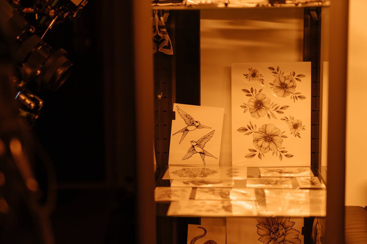 about-03 Tattoo sketches of birds and flowers displayed in a tattoo studio under warm lighting.