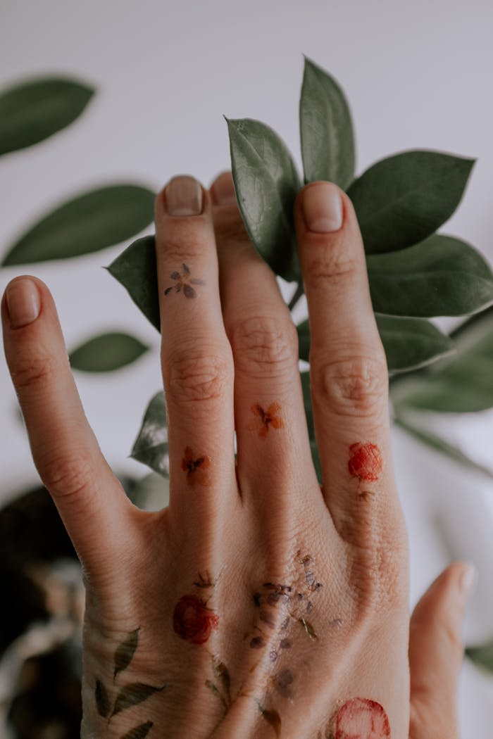 Close-up of a tattooed hand touching green leaves, showcasing nature and art.