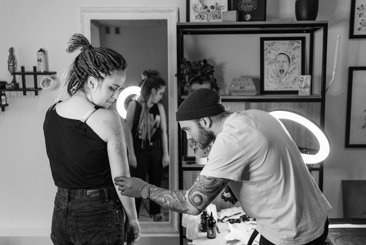 menu-09 Tattoo artist concentrates on creating a detailed design on a client's arm in a studio setting.